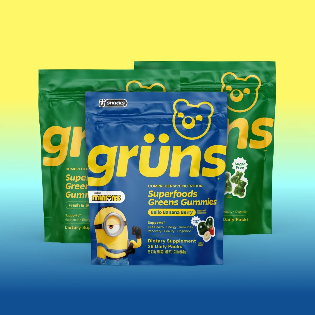 Three Grüns Superfoods Greens Gummies bags in green Original flavors and blue Bello Banana Berry with Minions branding, on a yellow-to-blue gradient background