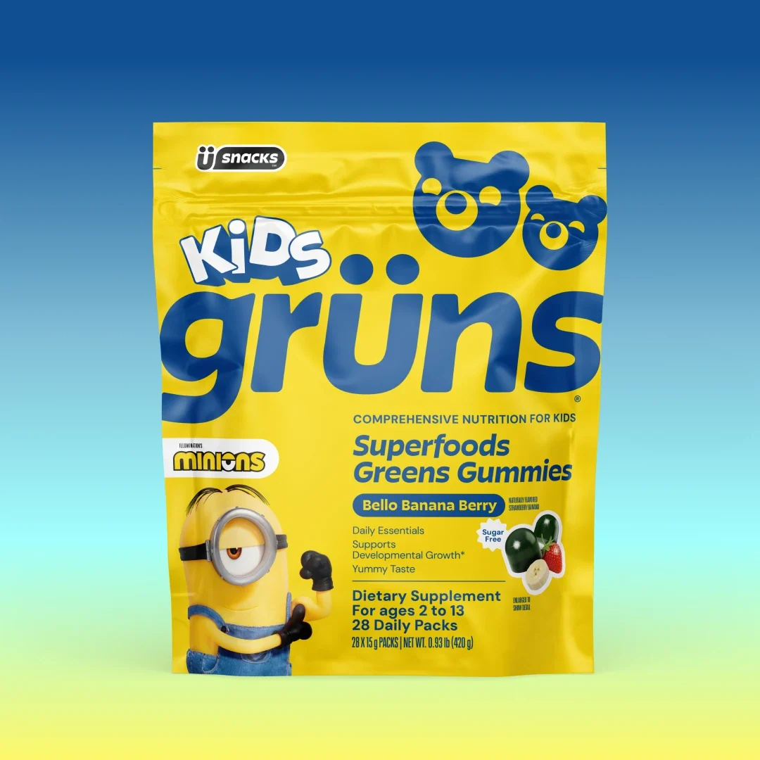 Yellow Kids Grüns Superfoods Greens Gummies bag in Bello Banana Berry flavor with Minions branding, on a blue-to-yellow gradient background