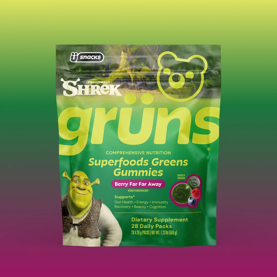 Green Grüns Superfoods Greens Gummies package featuring the Shrek logo and character, labeled Berry Far Far Away flavor, listing support for gut health, energy, immunity, recovery, beauty, and cognition, Dietary Supplement, 28 Daily Packs, on a green-to-purple gradient background.