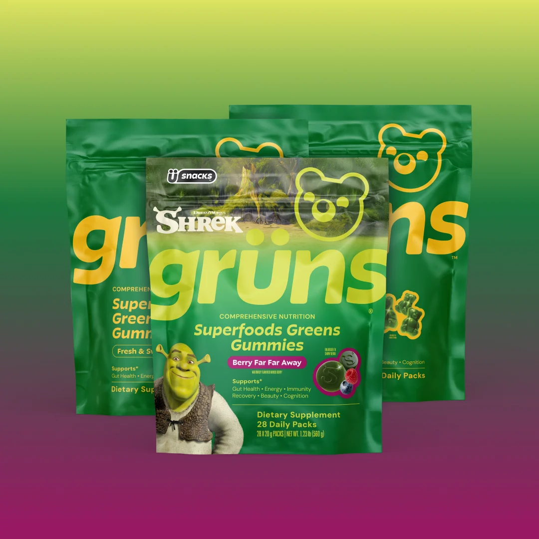 Three overlapping green Grüns Superfoods Greens Gummies packages, front pack featuring the Shrek character and labeled Berry Far Far Away flavor, on a green-to-purple gradient background.
