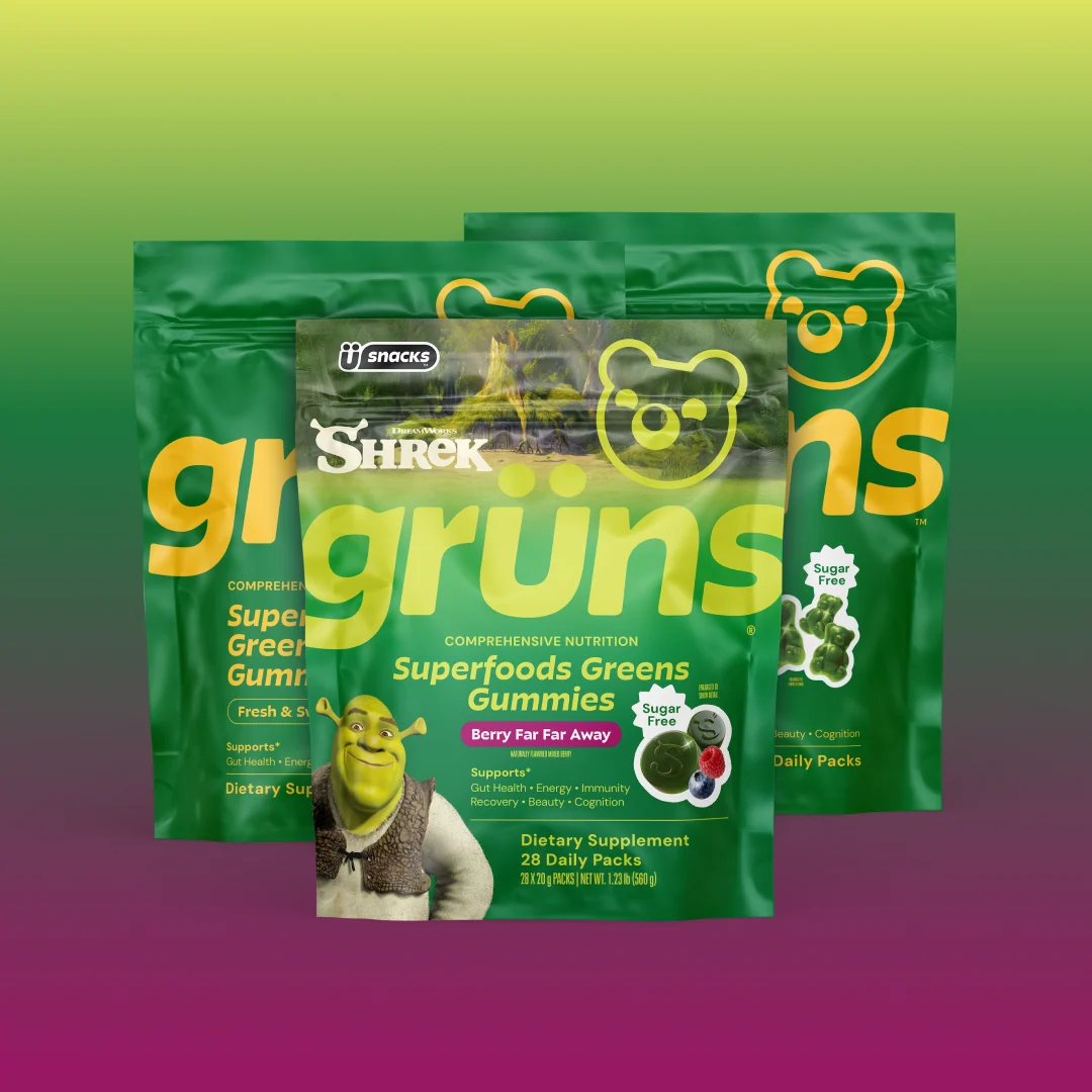 Three overlapping green Grüns Superfoods Greens Gummies packages, front pack featuring the Shrek character and labeled Berry Far Far Away flavor with a Sugar Free badge, on a green-to-purple gradient background.