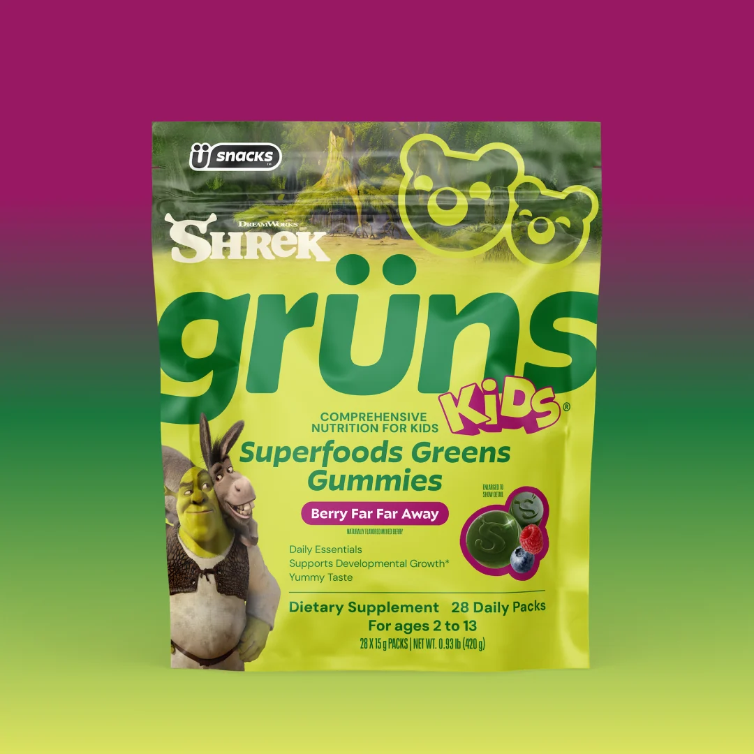 Yellow-green Shrek Kids Grüns Superfoods Greens Gummies package featuring Shrek and Donkey, labeled Berry Far Far Away flavor, listing Daily Essentials, Supports Developmental Growth, Yummy Taste, Dietary Supplement, 28 Daily Packs, for ages 2 to 13, on a purple-to-green gradient background.