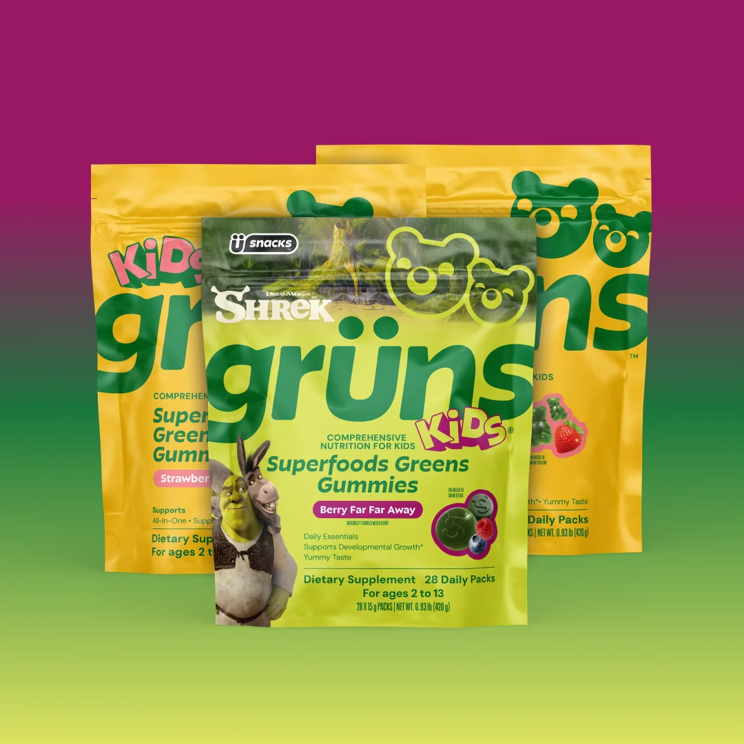 Three overlapping Kids Grüns Superfoods Greens Gummies packages, front pack featuring Shrek and Donkey and labeled Berry Far Far Away flavor, with yellow packs behind, on a purple-to-green gradient background.